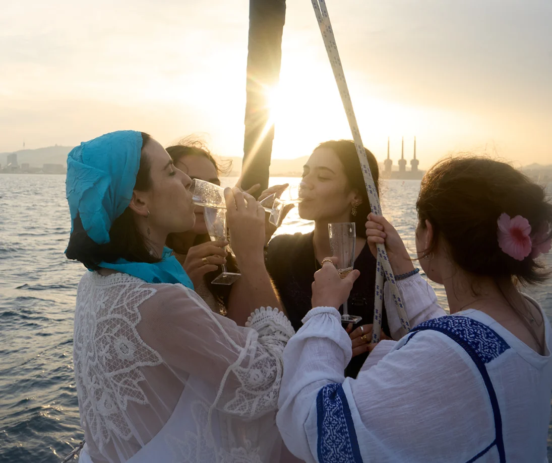 Tres personas hablando relajadas en un velero de lujo frente al skyline de Barcelona al atardecer