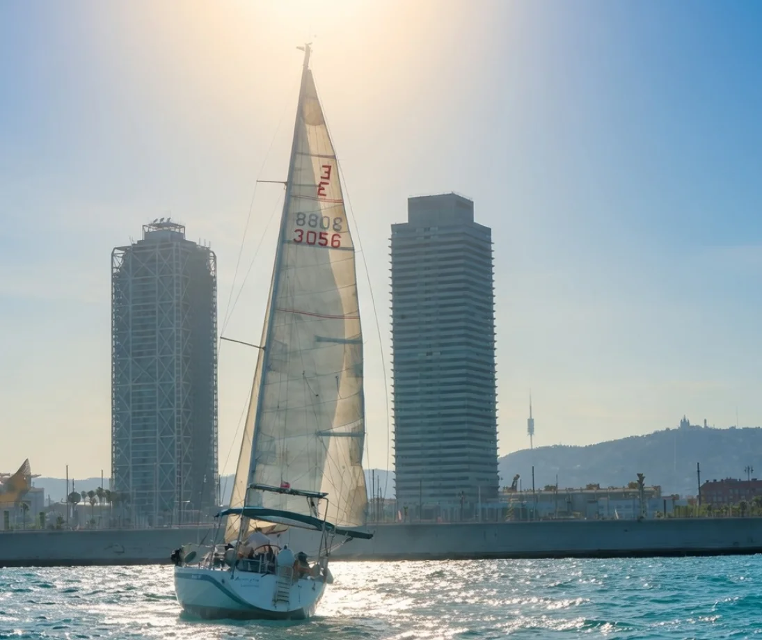 Tres persones parlant relaxadament en un veler de luxe davant l’skyline de Barcelona al capvespre