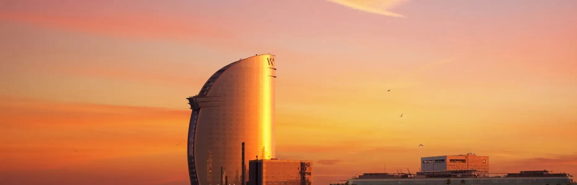 Amanecer daurat sobre l’hotel vela de Barcelona vist des del mar en un veler privat