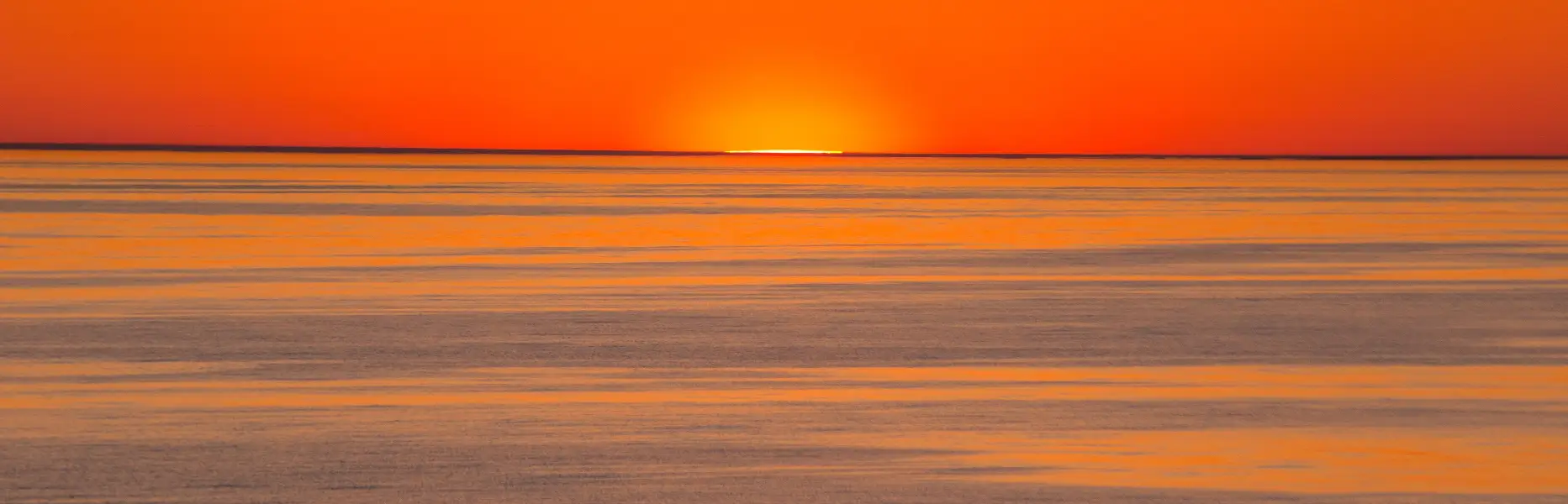 Salida del sol sobre el mar en calma con cielo naranja ideal para charter en velero al amanecer en Barcelona
