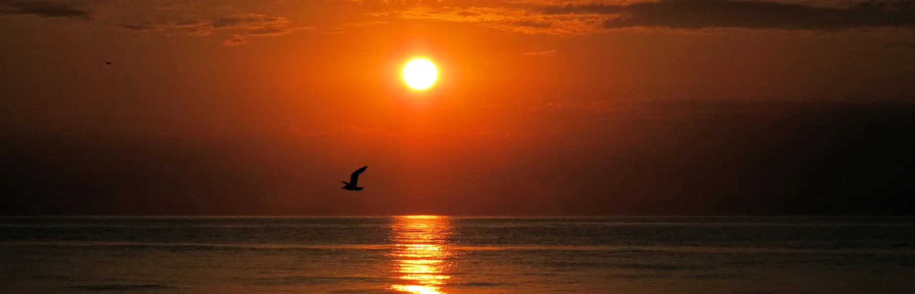 Sol naciendo sobre el mar en calma con un velero al amanecer frente a Barcelona