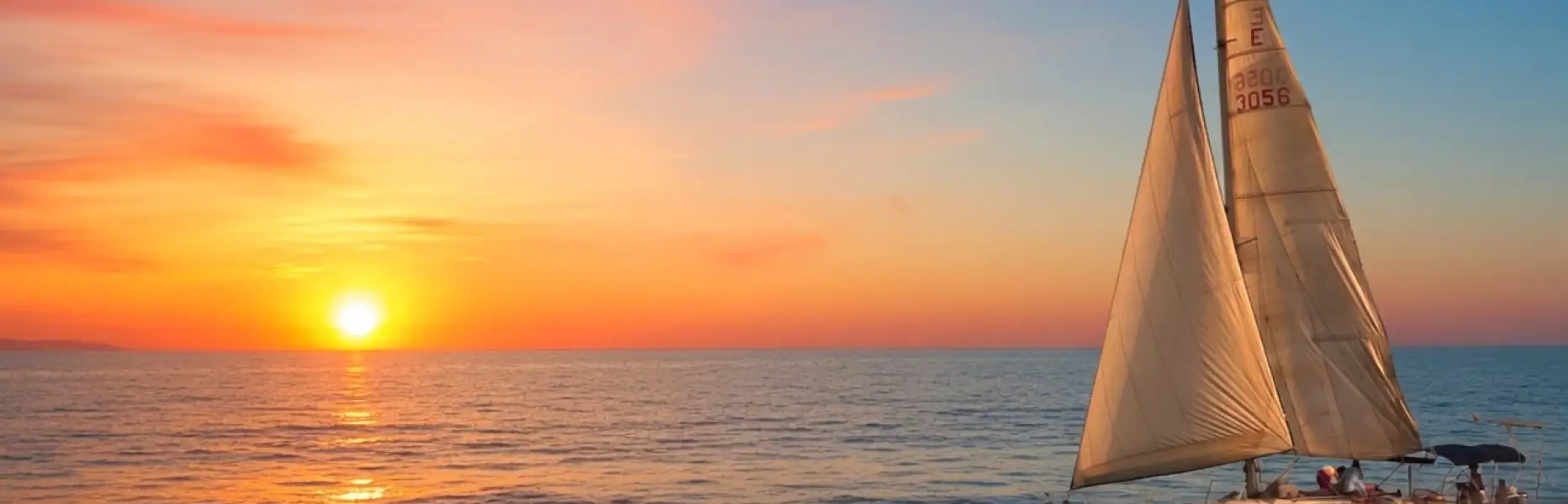 Barca a vela che naviga all’alba con il sole che sorge sul mare a Barcellona