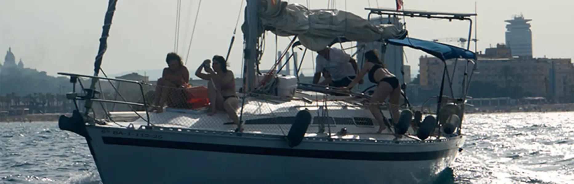 Grupo de personas disfrutando de un paseo en velero al atardecer frente a la costa de Barcelona