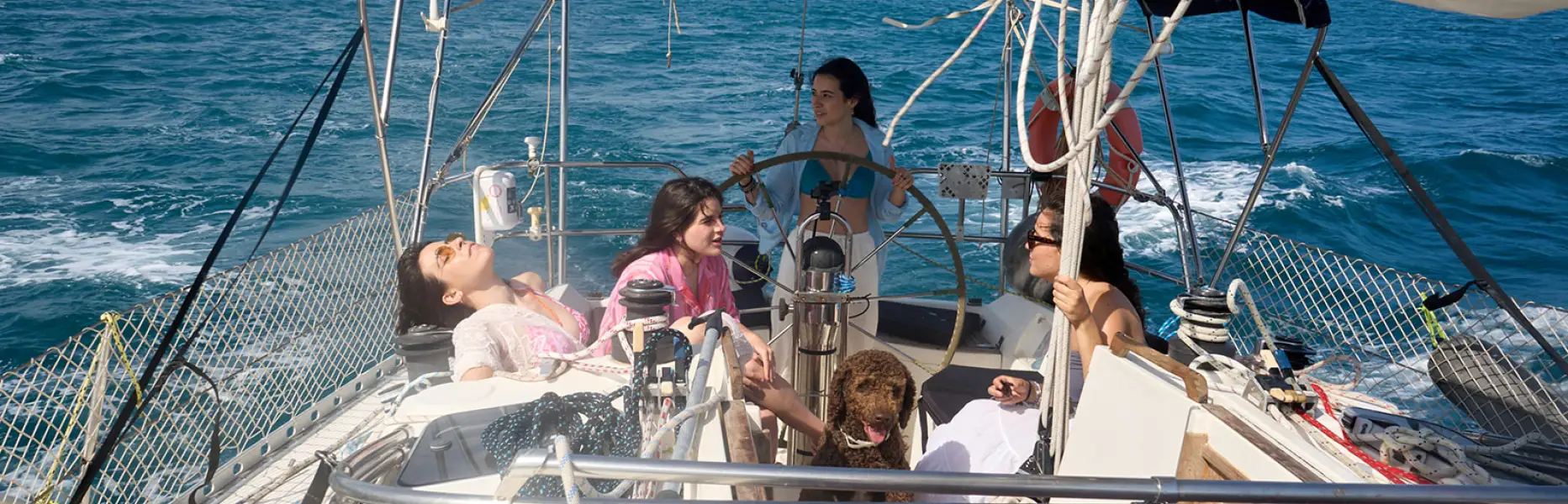 Grupo de amigas relajándose en la cubierta de un velero durante un charter privado frente a la costa de Barcelona