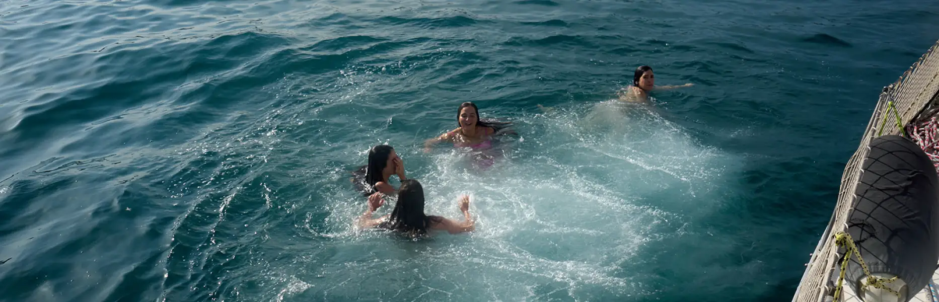 Mujer joven sonriendo mientras sostiene el timón de un velero en el mar con cielo despejado