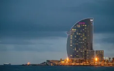 Vista dell'Hotel W di Barcellona al tramonto sul mare con le luci accese e il cielo nuvoloso