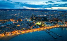 Luftaufnahme von Barcelona bei Sonnenuntergang mit Stadtlichtern und der erleuchteten Küste am Meer