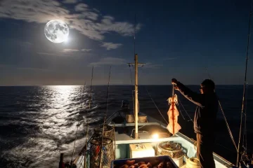 Pesca nocturna en barco bajo la luna llena