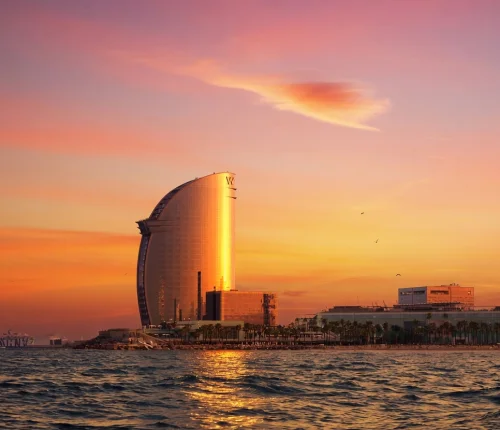 Amanecer dorado sobre el hotel vela de Barcelona visto desde el mar en un velero privado